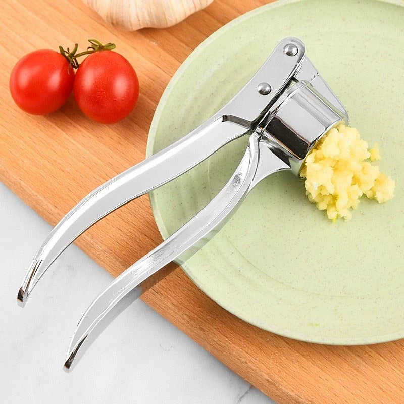 Garlic press with minced garlic on a green plate next to tomatoes on a wooden board